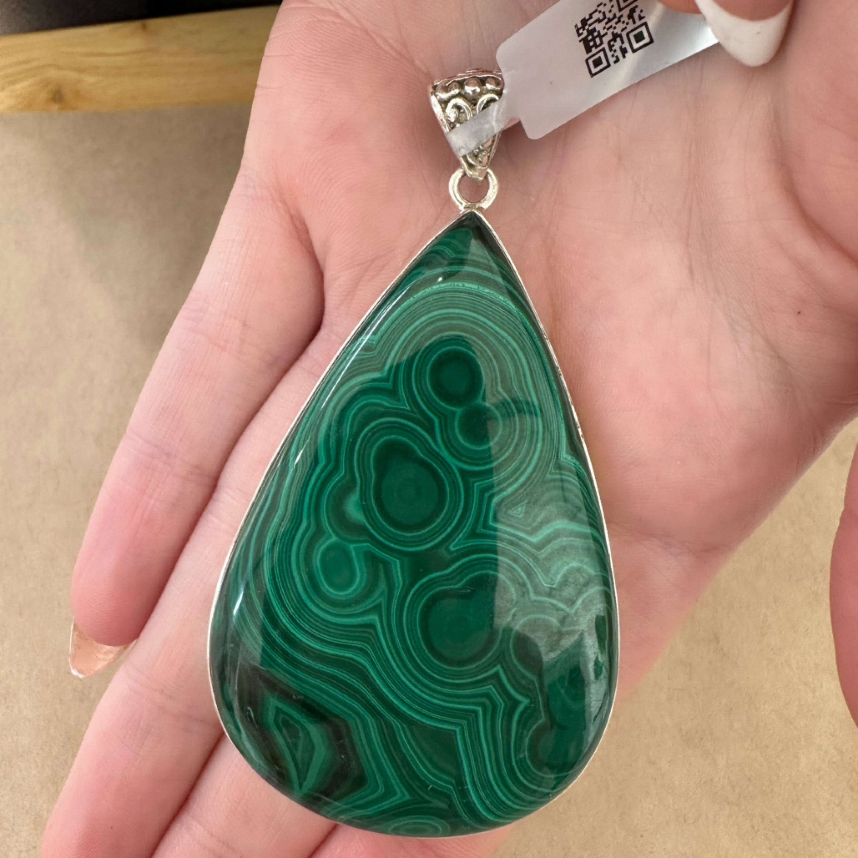 A hand holding out a spectacular malachite pendant in a large teardrop shop with a detailed finding at My Florist.