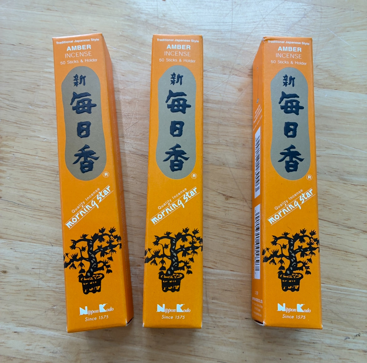Three orange boxes of Morning Star Amber incense sticks arranged side-by-side on a light wood surface.
