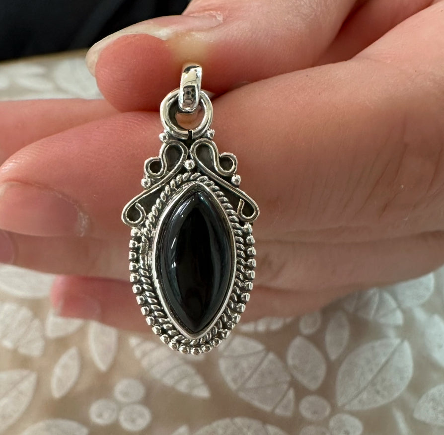 Vintage style Sterling Silver pendant with a black onyx stone held in a hand against a floral-patterned background