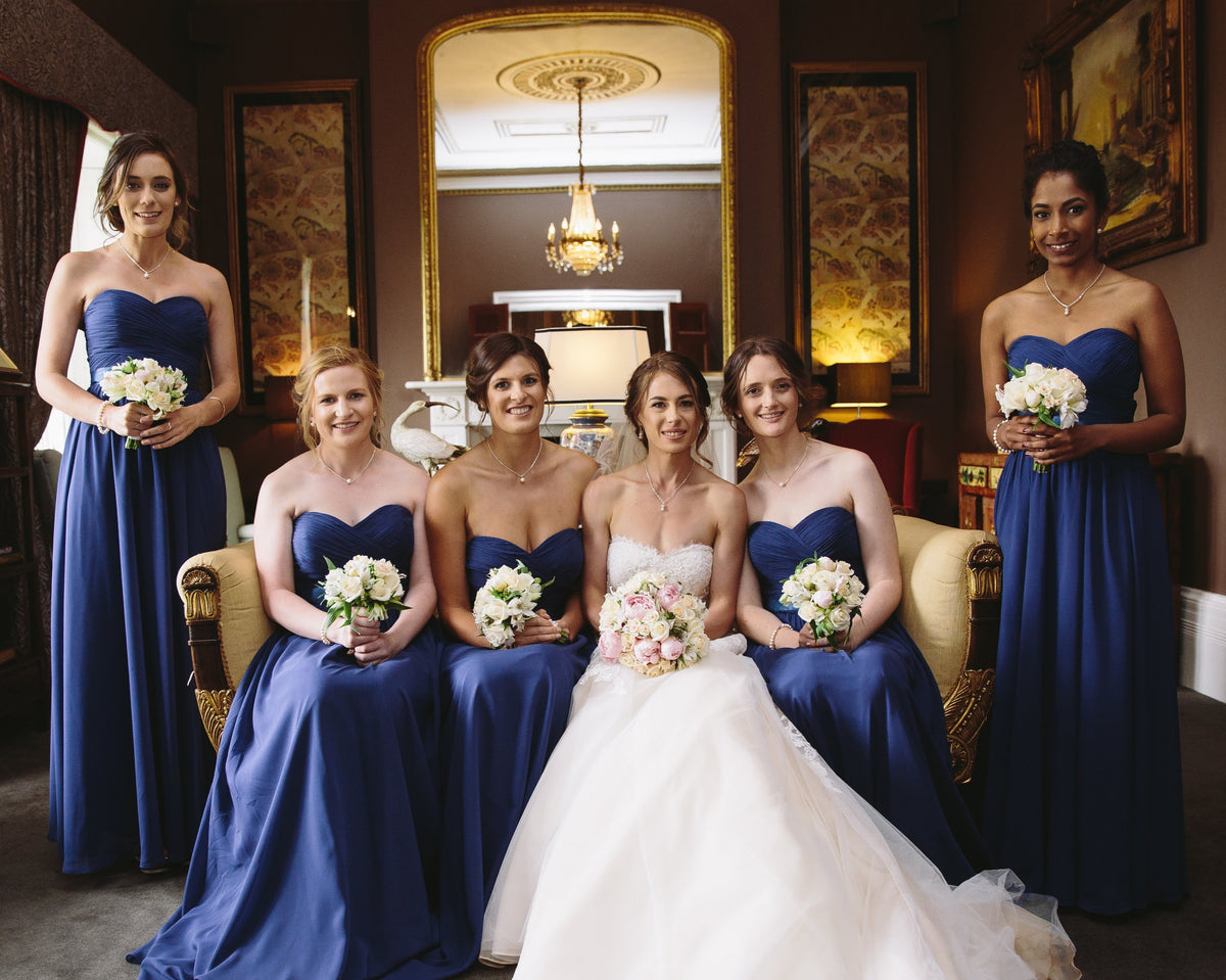 Bride in a white wedding gown with four bridesmaids in royal blue dresses holding white flower bouquets at Quamby Estate, Tasmania