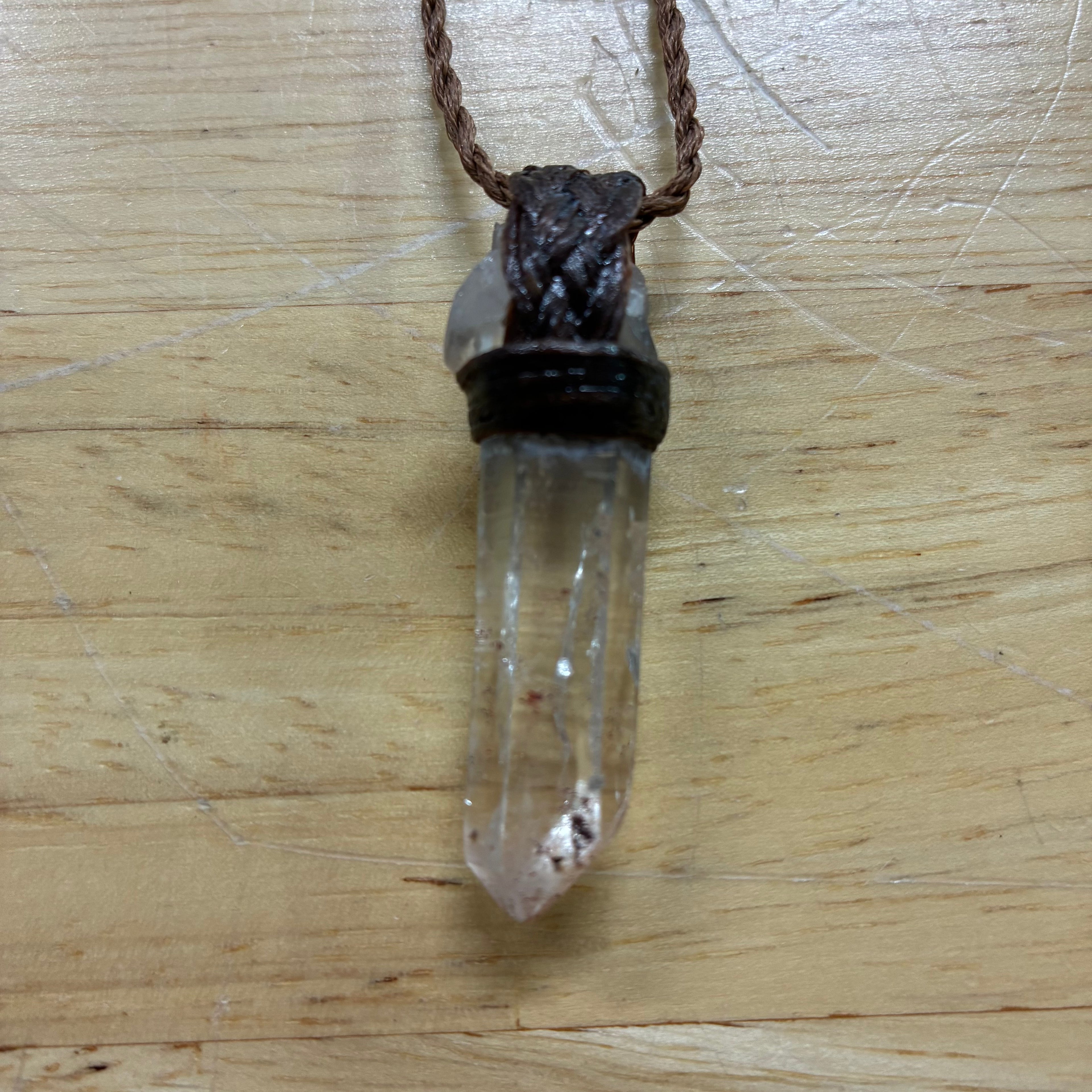Clear Quartz Leather Crystal pendant on a wooden surface