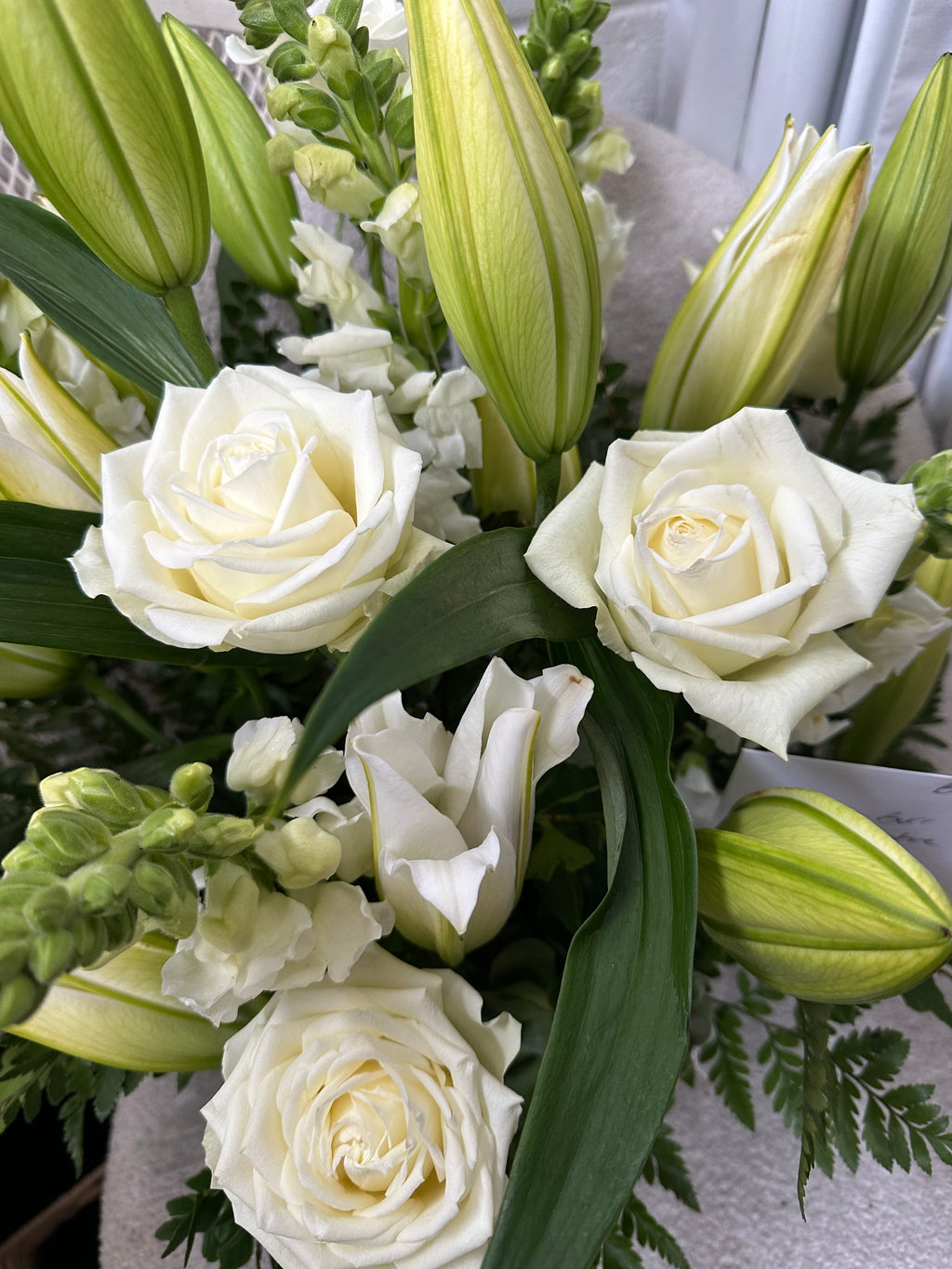 A close-up of a ceramic floral arrangement featuring white roses, white lily buds, and lush fern by your Launceston Florist