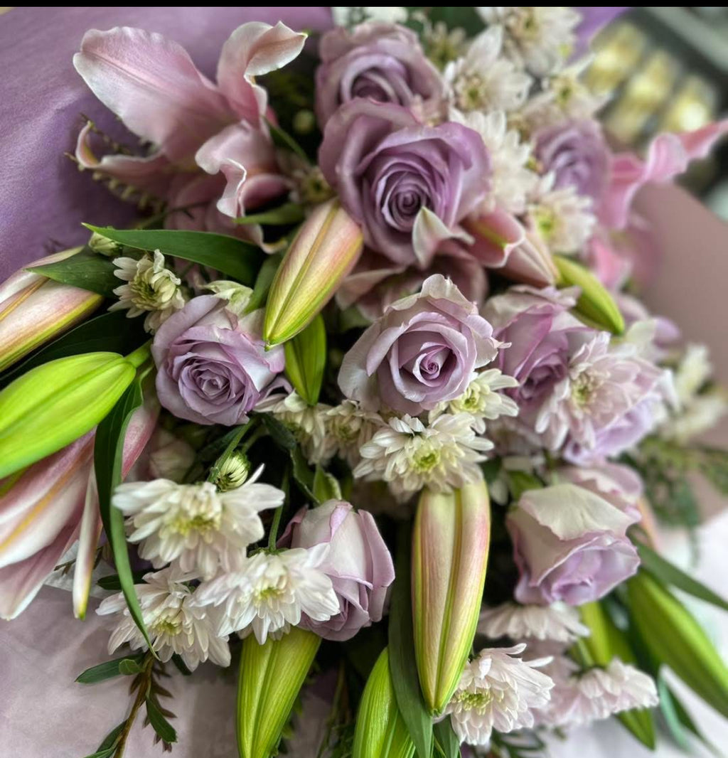 A close-up of a floral Sheaf featuring roses and lilies for sympathy flowers