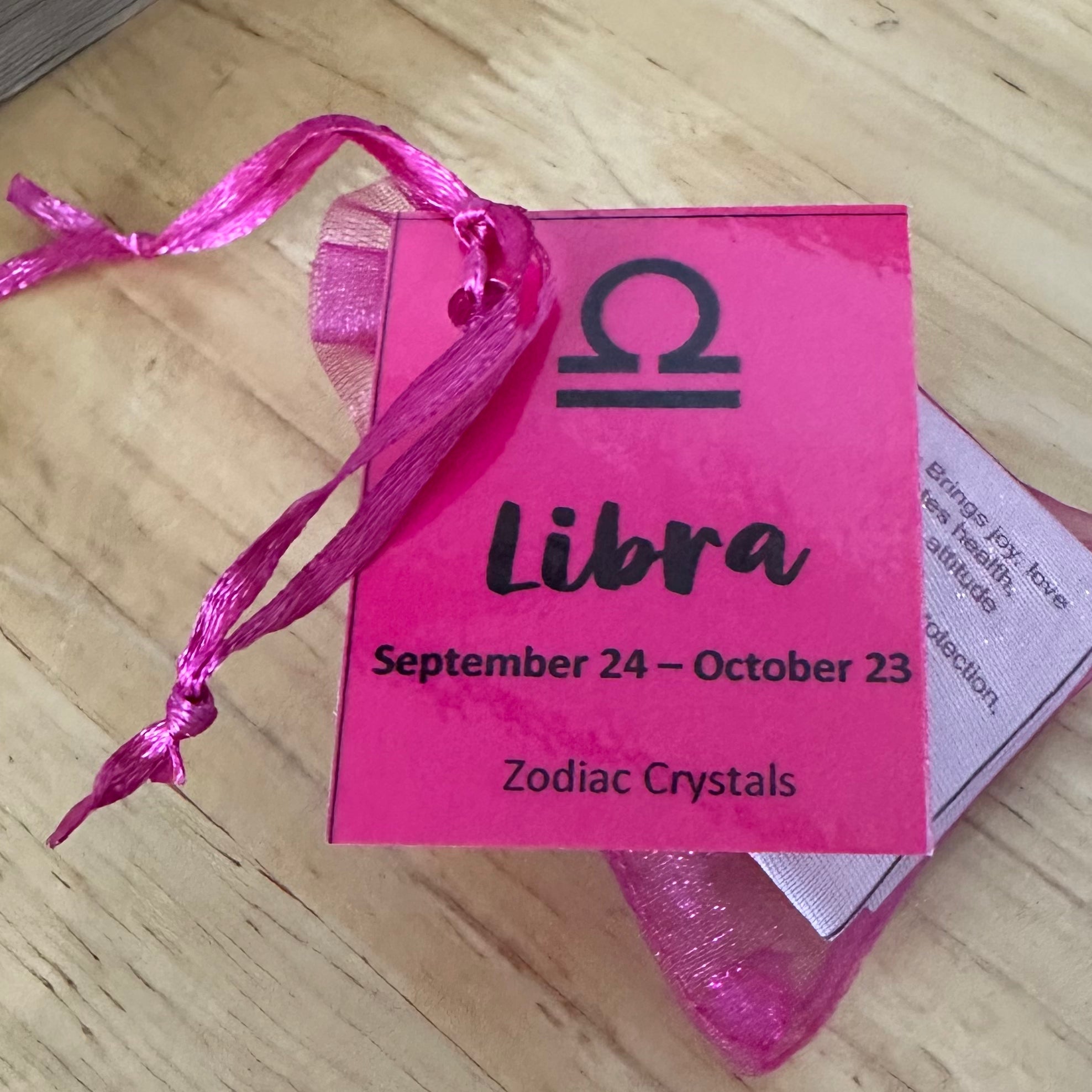 Pink organza bag with 'Libra' zodiac symbol and text on a wooden surface