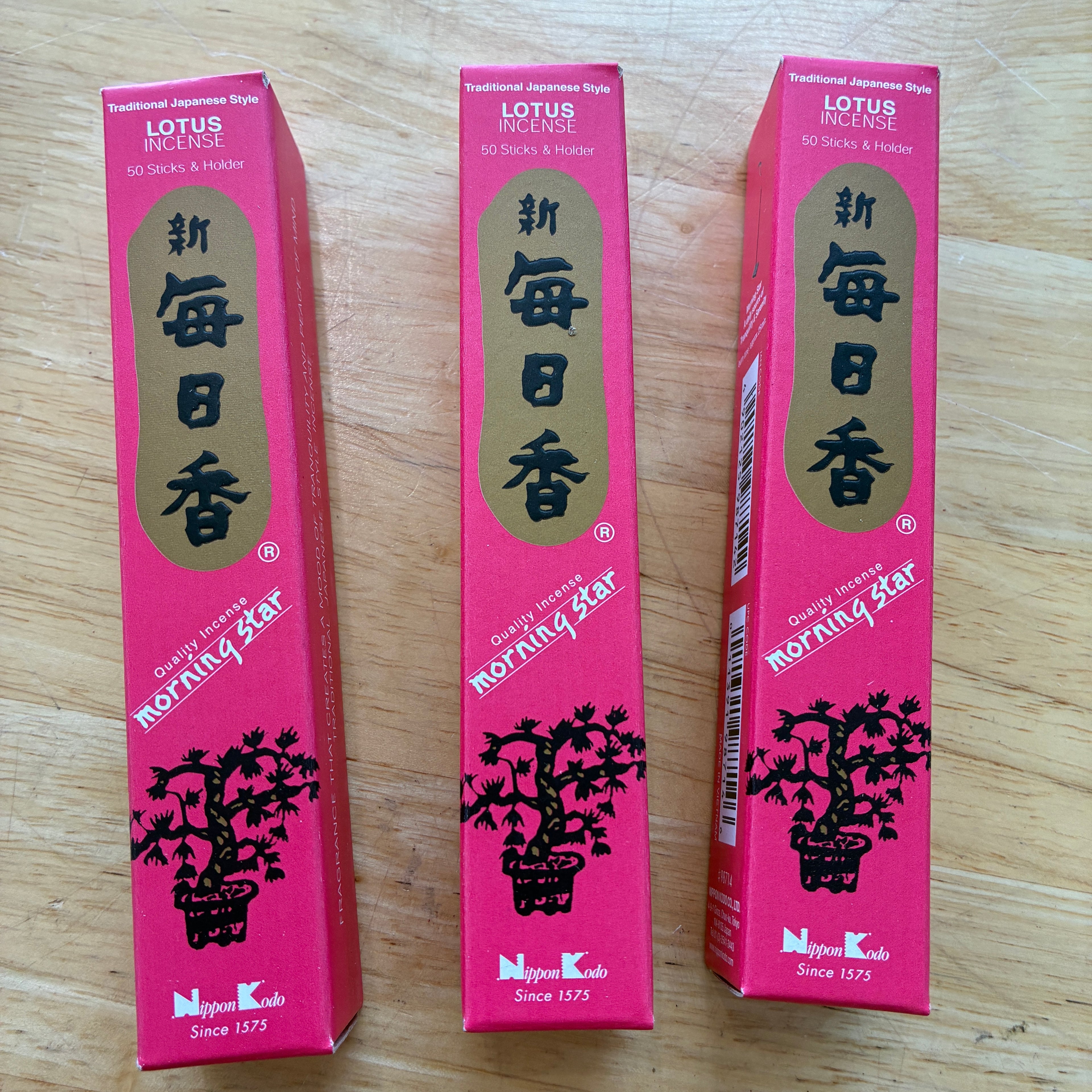 Three pink boxes of Lotus Morning Star incense sticks arranged side-by-side on a light wood surface.