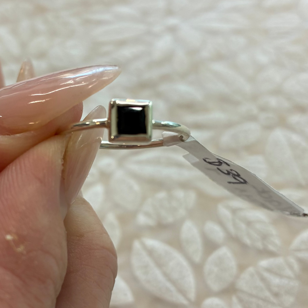 Square black onyx gemstone sterling Silver ring  held by a hand against a textured white background