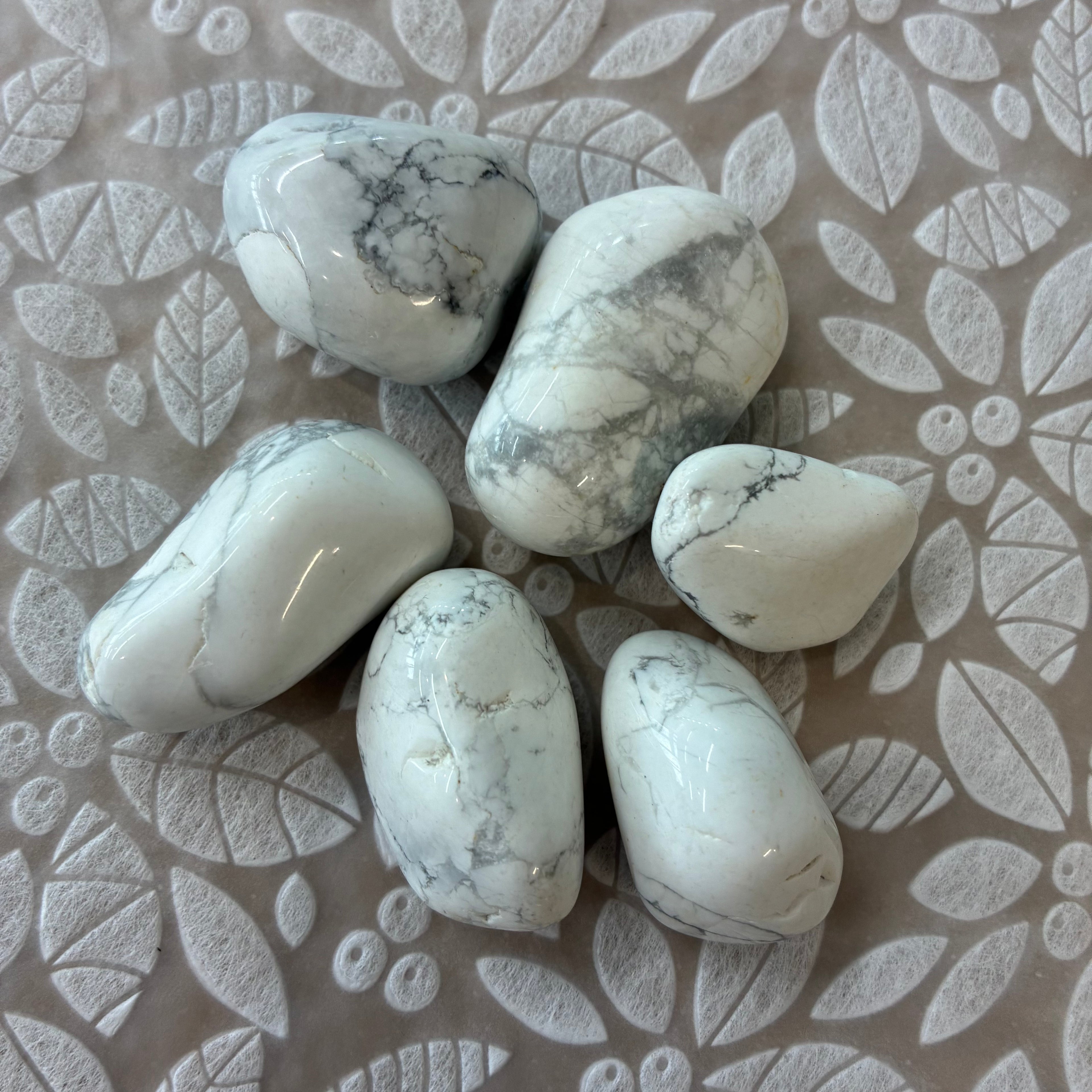 White howlite stones on a textured beige surface with leaf patterns