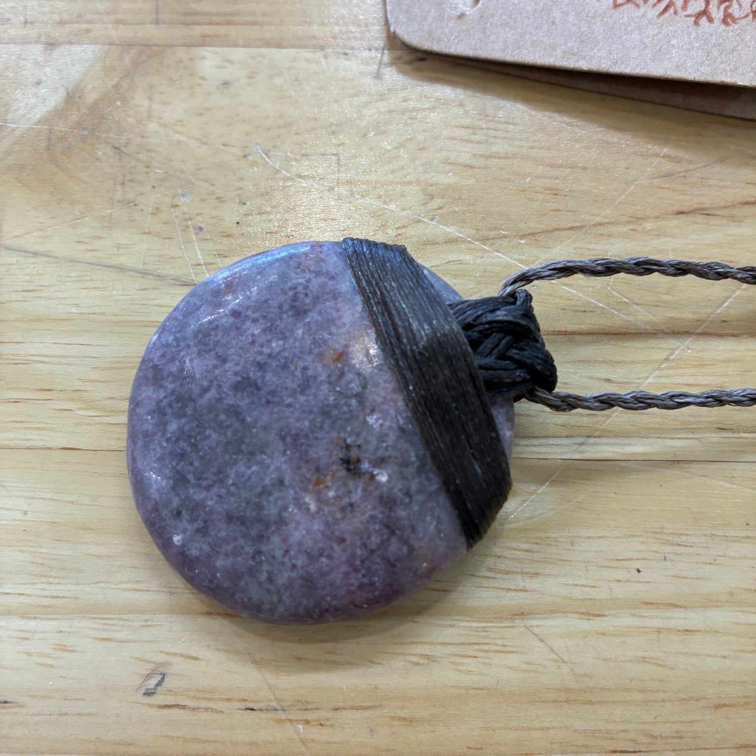Round purple lepidolite stone pendant on a string against a wooden background at Metaphysical Launceston