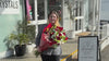 Florist walking outside the My Florist Launceston shop front in Launceston carrying a large delivery bouquet, passing a sandwich board sign with the business logo.